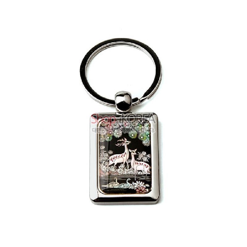 자개 상감 기법으로 흑색 바탕에 장생도 사슴과 학, 꽃문양을 섬세하게 표현한 금속 테두리 열쇠고리.