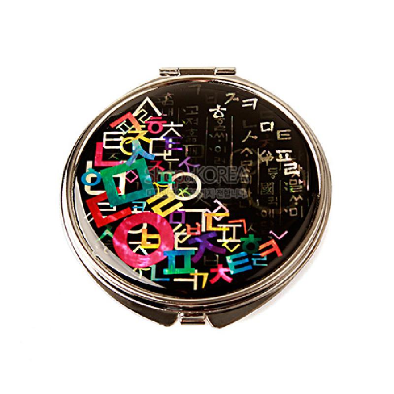 검은 옻칠 배경 위에 자개 상감으로 다채로운 한글 자모 문양을 배열한 원형 금속 손거울.