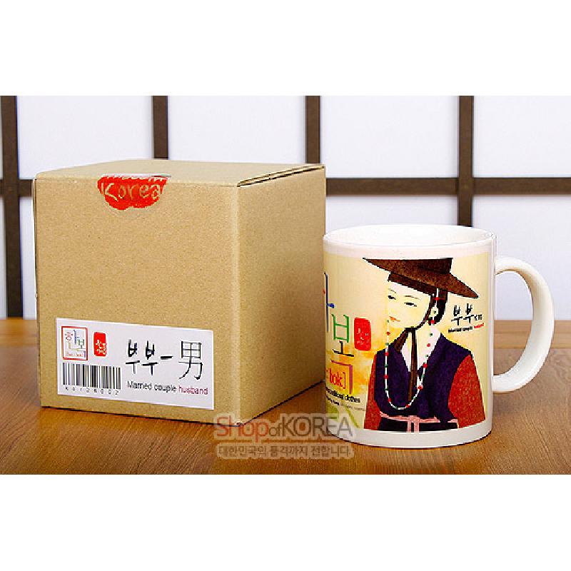 전통 한복과 갓을 착용한 남성 인물 일러스트가 인쇄된 세라믹 머그컵, 따뜻한 크림색 바탕과 붉은·남색 포인트 색상의 조화.