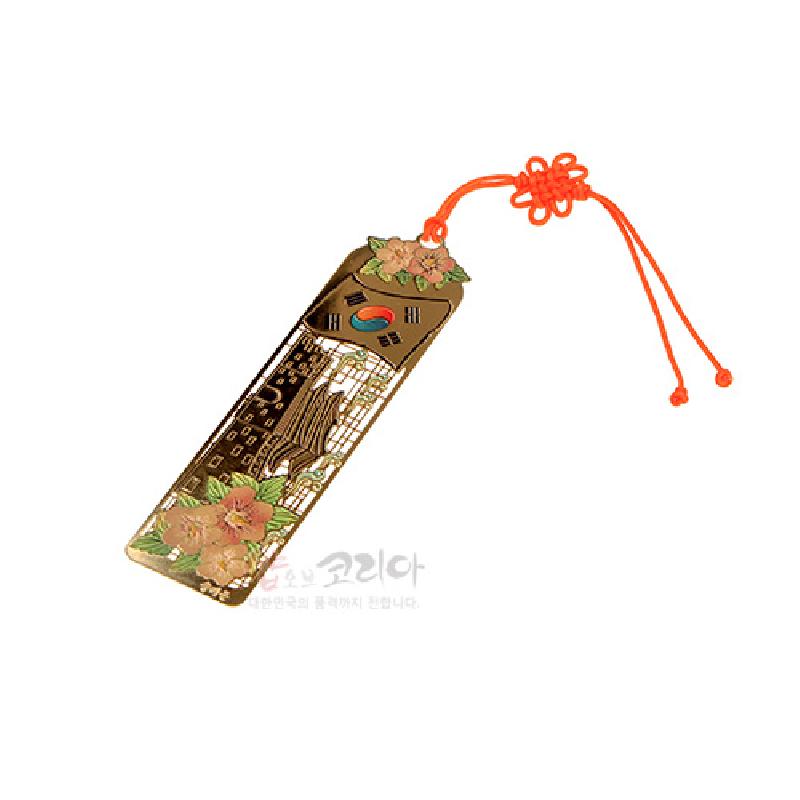 금속 재질에 금장 기법으로 남대문과 태극 문양을 새기고 분홍 무궁화와 주황색 매듭 끈 장식을 더한 책갈피.