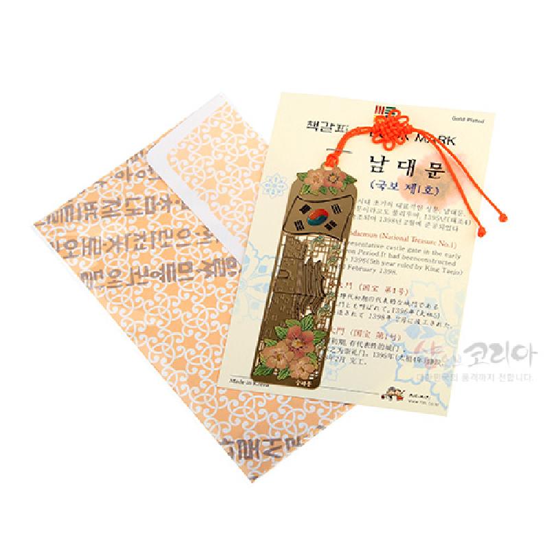 금속 재질에 남대문 전경을 섬세하게 음각하고, 태극기와 꽃문양, 주황색 매듭 끈 장식이 조화를 이룬 책갈피.