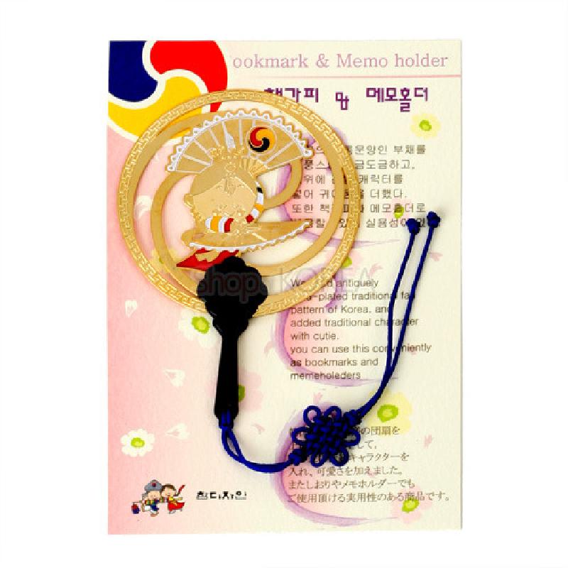 부채춤 인물이 새겨진 금속 원형 장식과 전통 문양 테두리, 청색 매듭 끈 장식의 메모홀더 겸 책갈피.