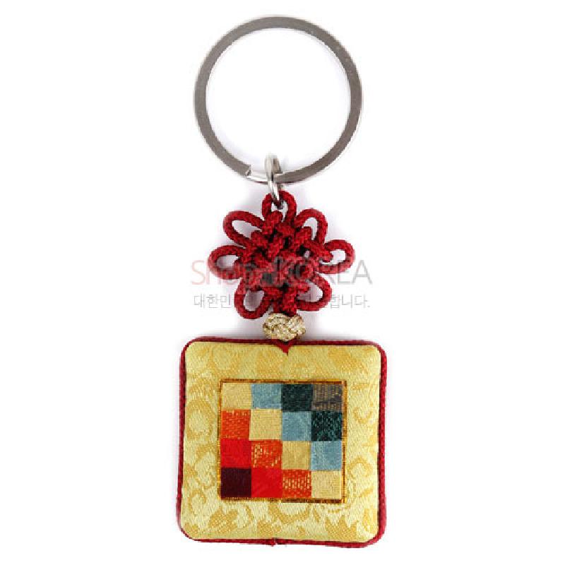 황색 비단 바탕에 다채로운 조각보 누비 문양이 더해진 사각 장식과 붉은 전통 매듭이 연결된 금속 고리 열쇠고리.