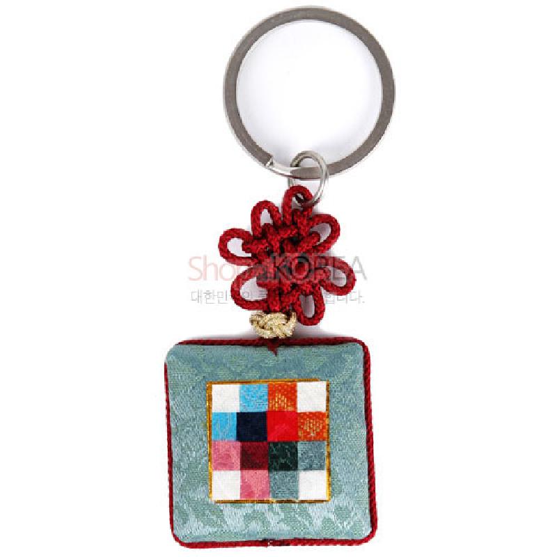 옥색 비단 바탕에 다색 조각보 패턴이 수놓인 방석형 패드와 붉은 전통 매듭 장식이 달린 금속 고리 열쇠고리.