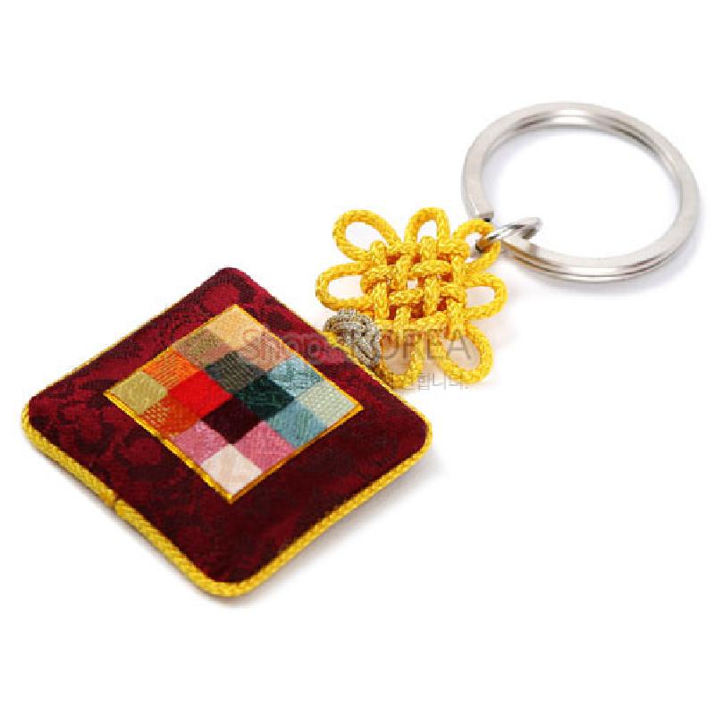 자주색 바탕에 다채로운 비단 조각보 누빔 장식과 노란 전통 매듭, 금속 고리가 조화된 열쇠고리.