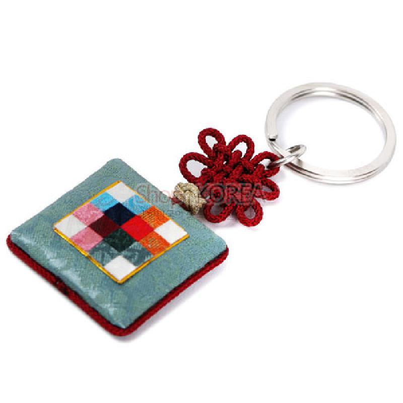 옥색 비단 바탕에 다채로운 조각보 패턴이 더해진 방석형 장식과 붉은 전통 매듭, 금속 고리가 조화된 열쇠고리. 옥색 비단 바탕에 다채로운 조각보 패턴이 더해진 방석형 장식과 붉은 전통 매듭, 금속 고리가 조화된 열쇠고리.