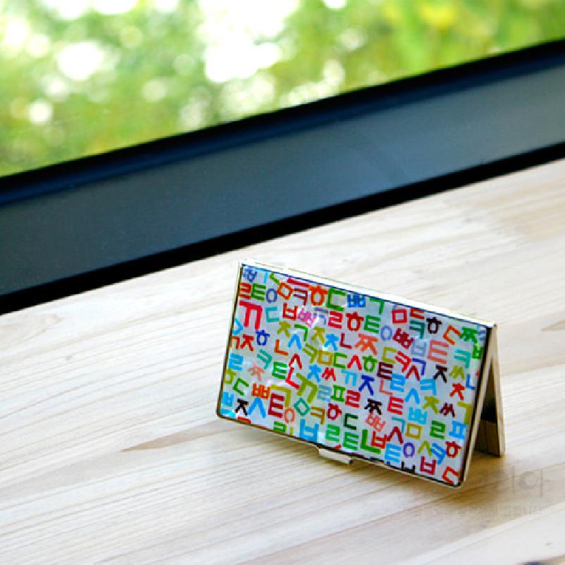 흰 바탕 위에 다채로운 색상의 한글 자음 패턴을 인쇄한 금속 재질 명함케이스.