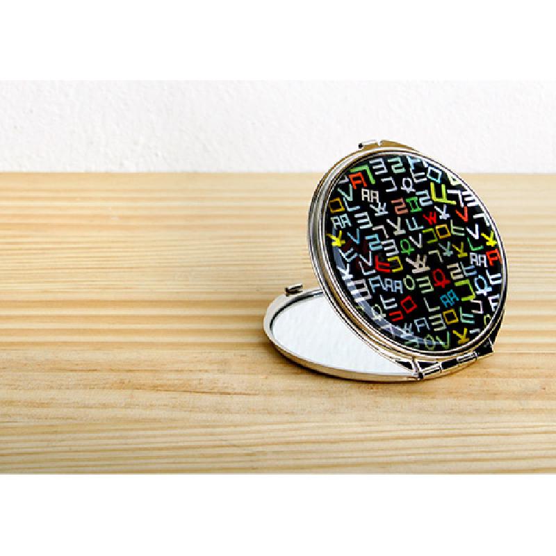 검은 바탕 위에 다채로운 색상의 훈민정음 자음 문양이 인쇄된 금속 테두리 접이식 손거울.