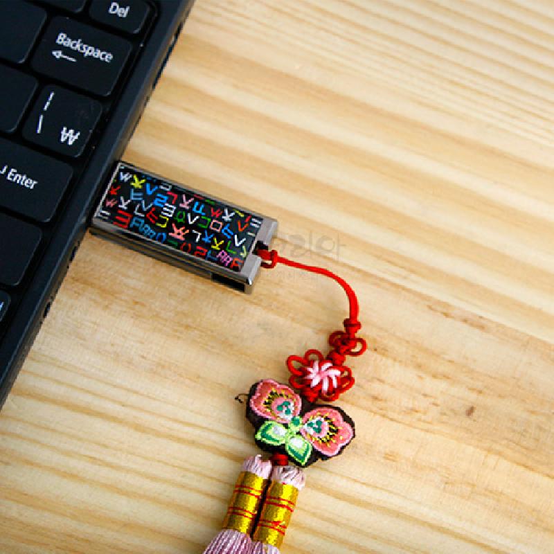 흑색 바탕에 형형색색 훈민정음 자음 문양이 들어간 금속 USB와 나비 자수 비단매듭 장식.