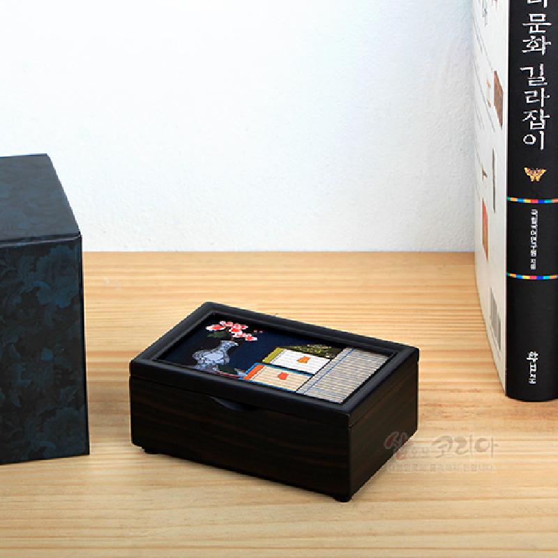 짙은 나무결 상자 위에 옻칠 바탕과 자개 상감으로 책가도와 꽃, 병 문양을 섬세하게 표현한 직사각 명함함.