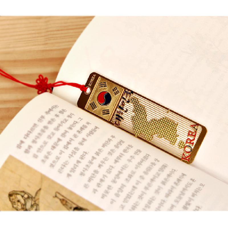 금속 재질에 태극 문양과 사각형 패턴의 한반도 지도가 양각된 금장 책갈피, 붉은 매듭끈 장식.