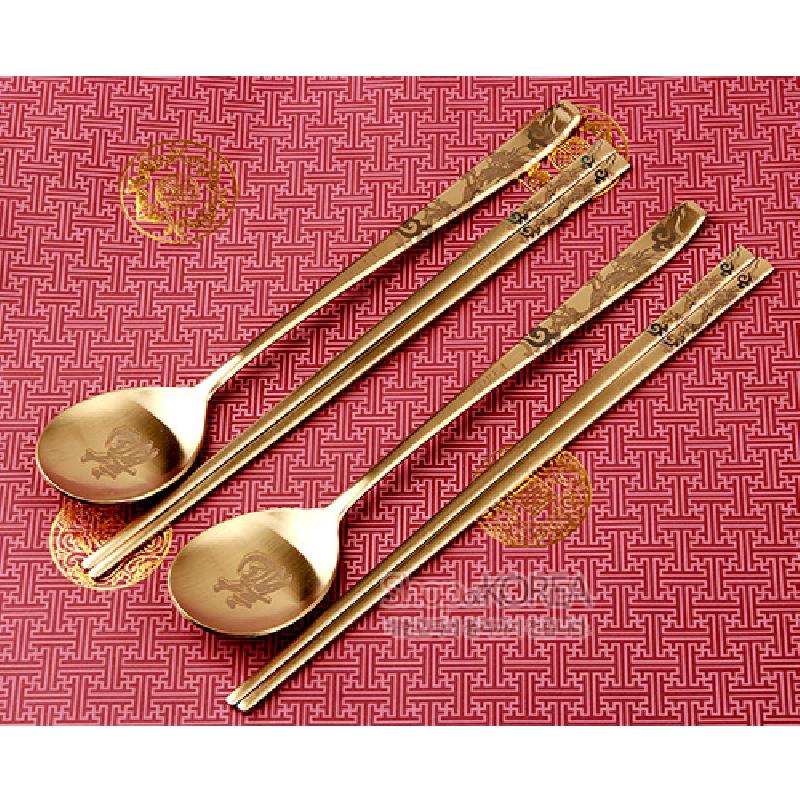 금빛 티타늄 소재에 용 문양이 새겨진 수저와 젓가락 2인 세트, 붉은 전통 기하무늬 배경의 금색 포인트 장식.