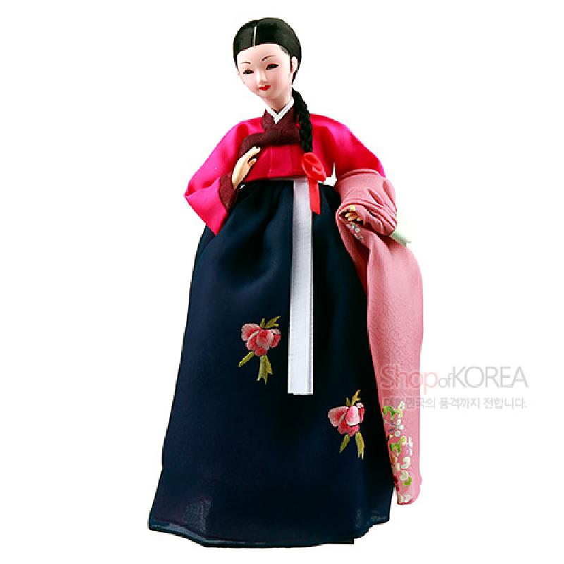 비단 느낌의 소재로 제작된 한복 인형, 진분홍 저고리와 남색 치마에 꽃 자수 문양과 분홍색 자수 손수건 장식이 특징인 장식 인형.
