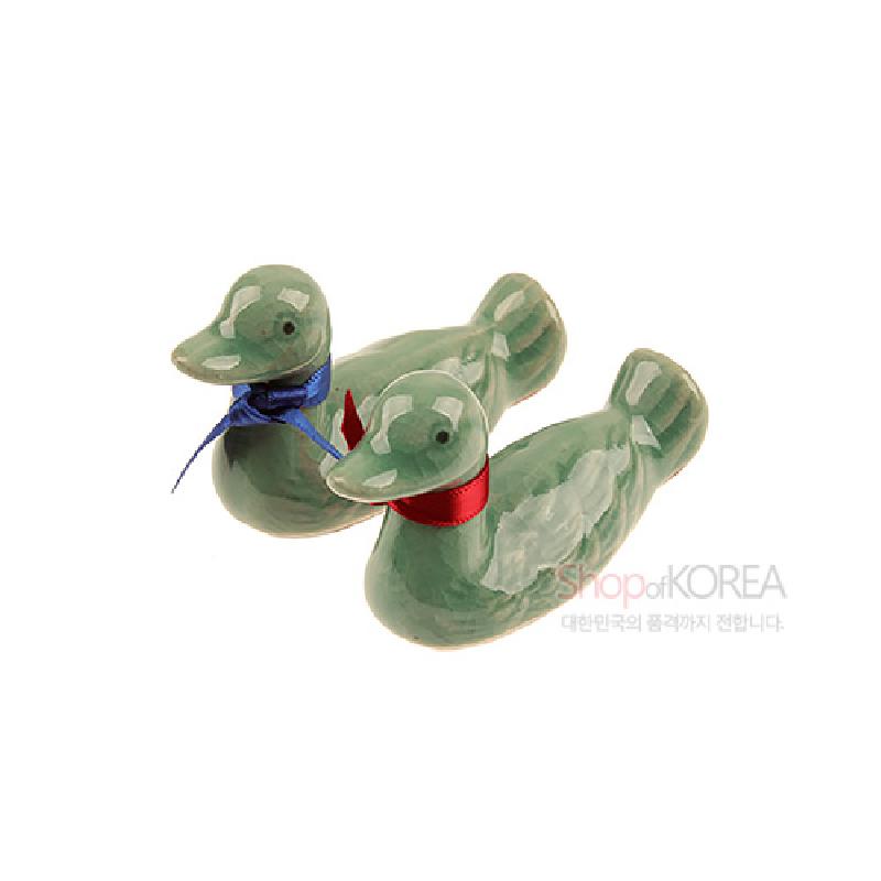 청자 재질의 윤기 나는 원앙 형태 수저받침에 청색·홍색 리본 장식이 더해진 한쌍 구성.