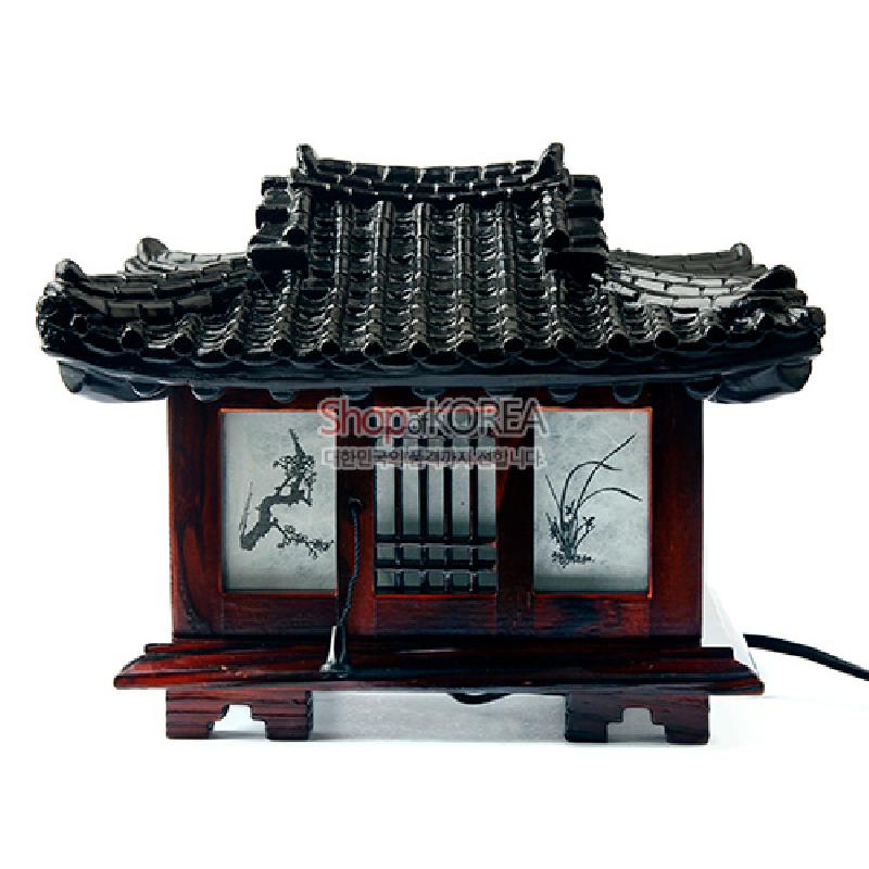 짙은 갈색 목재와 검은 기와 지붕으로 형상화된 한옥 형태, 창호에 수묵화 식물 문양이 더해진 좌등 스탠드.