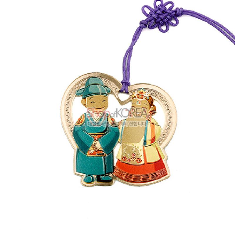 금속 재질 하트형 틀에 전통 혼례복을 입은 신랑·신부 캐릭터가 채색된 디자인과 보라색 매듭 끈 장식 책갈피.