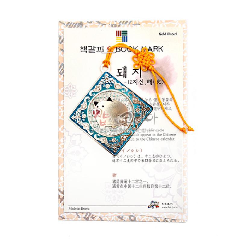 금속 재질에 금장 처리된 사각 장식과 돼지 12지신 문양, 청록색 에나멜 배경과 노란색 전통 매듭 끈이 조화를 이룬 책갈피.