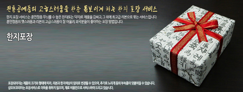 [텍스트: 전통공예품의 고급스러움을 한층 돋보이게 하는 한지 포장 서비스 / 한지포장] 한지 문양 포장지와 붉은 금색 리본 장식, 전통 서체 인쇄가 어우러진 선물 상자 이미지